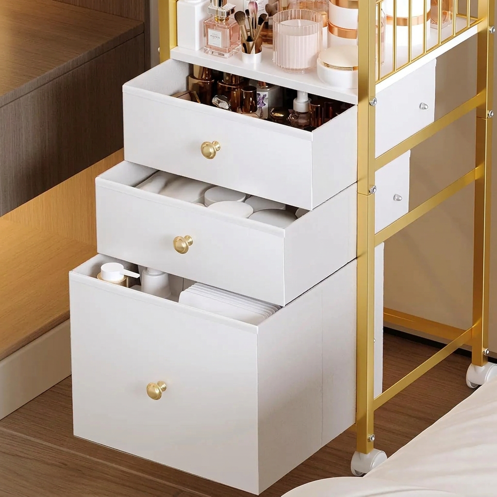 Three white fabric drawers with gold knobs on the rolling makeup organizer cart